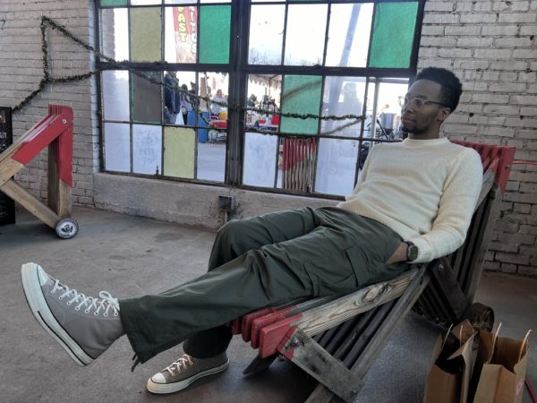 Malik relaxing in a wooden lounge chair in a cream sweater