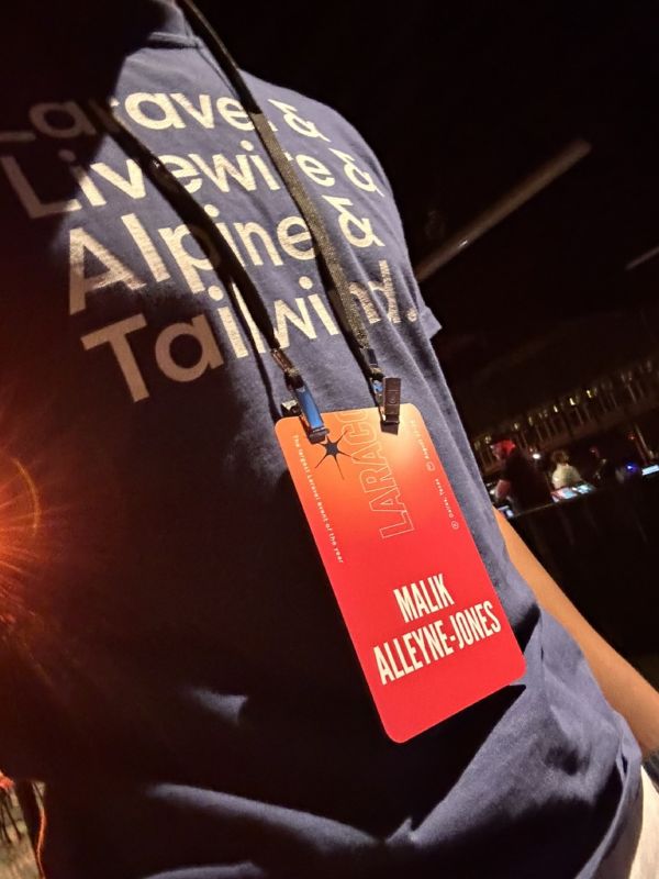 Laracon conference badge reading Malik Alleyne-Jones, worn over a Laravel, Livewire, Alpine, and Tailwind t-shirt
